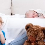 mom smiling at her toddler and newborn sleeping